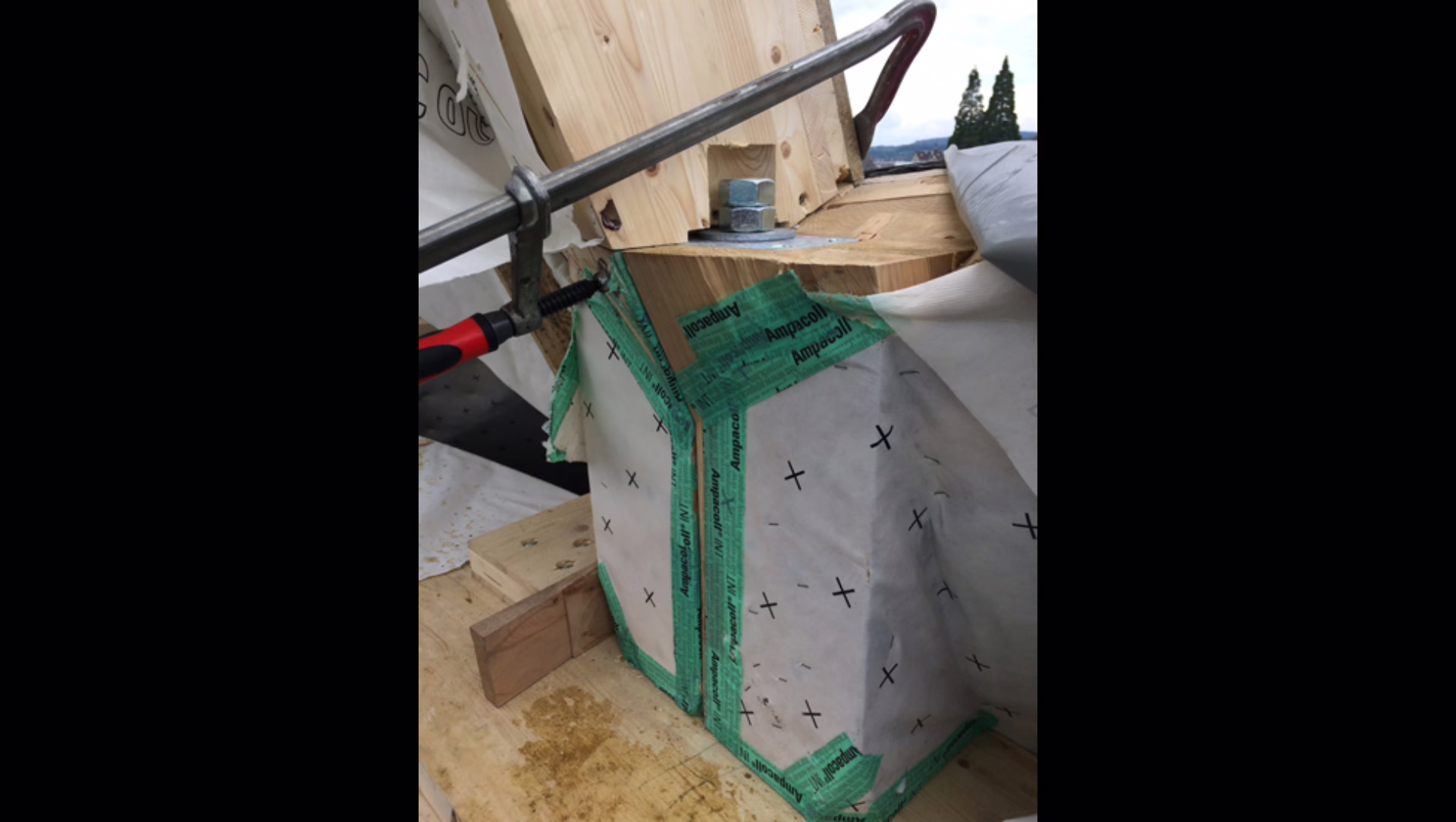 Detailaufnahme Elementstoss am ersten Druckring (Holzfläche unten im Bild). Mit Luftdichheitsfolie abgeklebt sind die Konsolhölzer, auf denen die grossen Dachelemente auf dem Druckring aufgelegt werden konnten, ersichtlich. Der Druckring ist durch die grossen M30er-Bauschrauben auf Drucknormalkraft an den Dachelementen aufgehängt. Oberhalb der Schraube ist der Hornholzkontaktstoss der zweiten Elementebene zu sehen.