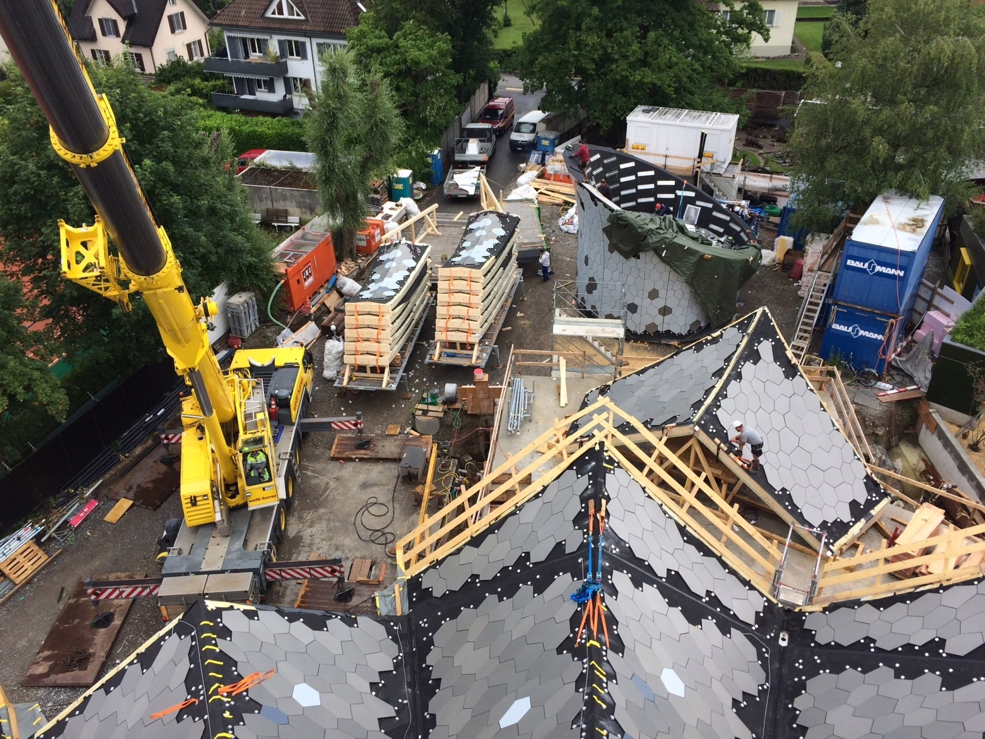 Logistische Herausforderungen mit beengten Platzverhältnissen. Während die Vordachelemente versetzt werden, werden die Elemente für den die zweite Elementebene angeliefert. Im Hintergrund sind die Spenglerarbeiten am «Hut» im Gange, welcher schon bald auf das Gebäude aufgesetzt wird.