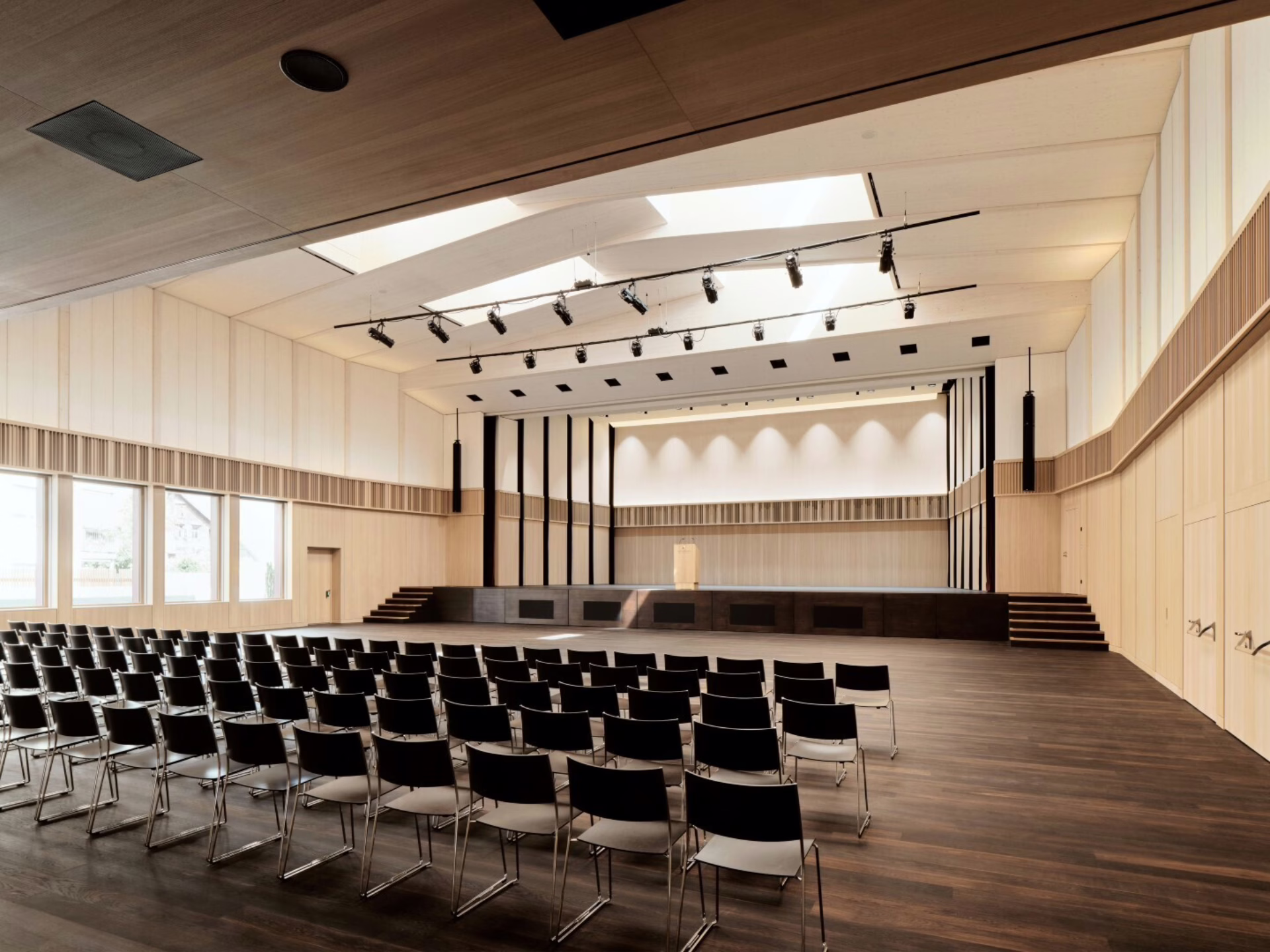 Variable Raumakustik: Der Löwensaal besteht aus sichtbaren HolzoberflĂ€chen, und es konnten verschiedene Akustikmassnahmen umgesetzt werden. Die oberen Bereiche der SeitenwĂ€nde sind mit drehbaren, akustisch unterschiedlich wirksamen Wandfronten ausgefĂŒhrt â einerseits schallreflektierend und andererseits schallabsorbierend. Mit AkustikvorhĂ€ngen auf der BĂŒhne, an der Aussenwand im Erdgeschoss vor den Fenstern und unterhalb der Galerie kann gemĂ€ss WĂŒnschen der Musiker die Akustik halliger oder trockener eingestellt werden. Foto: Ladina Bischof Fotografie.
